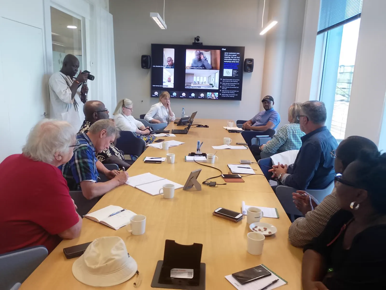 Forum participants in a working session with remote partners visible on a screen